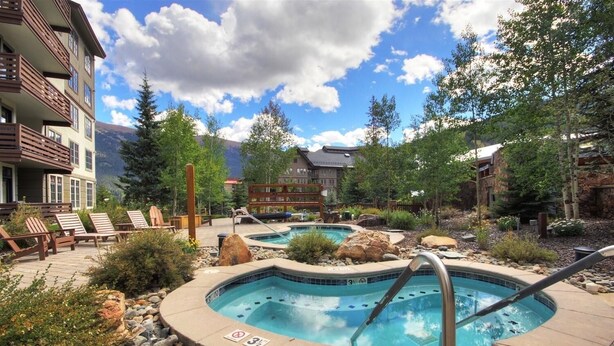 A resort with a hot tub area, lounge chairs, and a pool surrounded by rocks and plants.