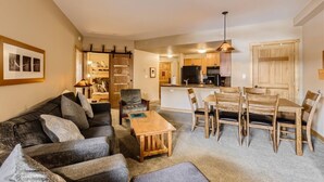 A modern living room with a sofa, coffee table, and dining area with wooden chairs and a table.