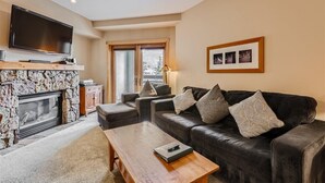 A living room with a stone fireplace, a leather sofa, a wooden coffee table, and a flat-screen TV mounted above the fireplace.