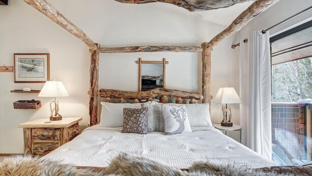 Une chambre à coucher au décor rustique, comprenant un lit avec une tête de lit en bois, deux tables de chevet avec des lampes et un grand miroir au-dessus du lit.