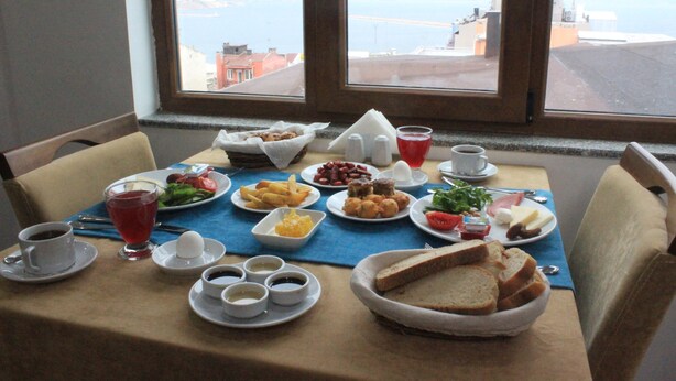 A breakfast table with various dishes, cups, and a view of the sea through the window. - Grand Serenay Hotel (Bandirma)