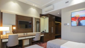 Une chambre d’hôtel avec deux lits, un bureau, une chaise, une télévision, un miroir et un tableau au mur.