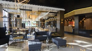 Un hall d’entrée spacieux au design moderne, comprenant un espace détente avec des canapés et une table basse, un comptoir d’accueil et un escalier menant aux étages supérieurs.