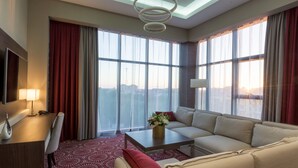 Une chambre d’hôtel moderne dotée d’une grande fenêtre, d’un canapé, d’une table basse et d’un bureau avec une lampe.