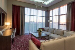 Una habitación de hotel moderna con un ventanal grande, un sofá, una mesa de centro y un escritorio con lámpara.
