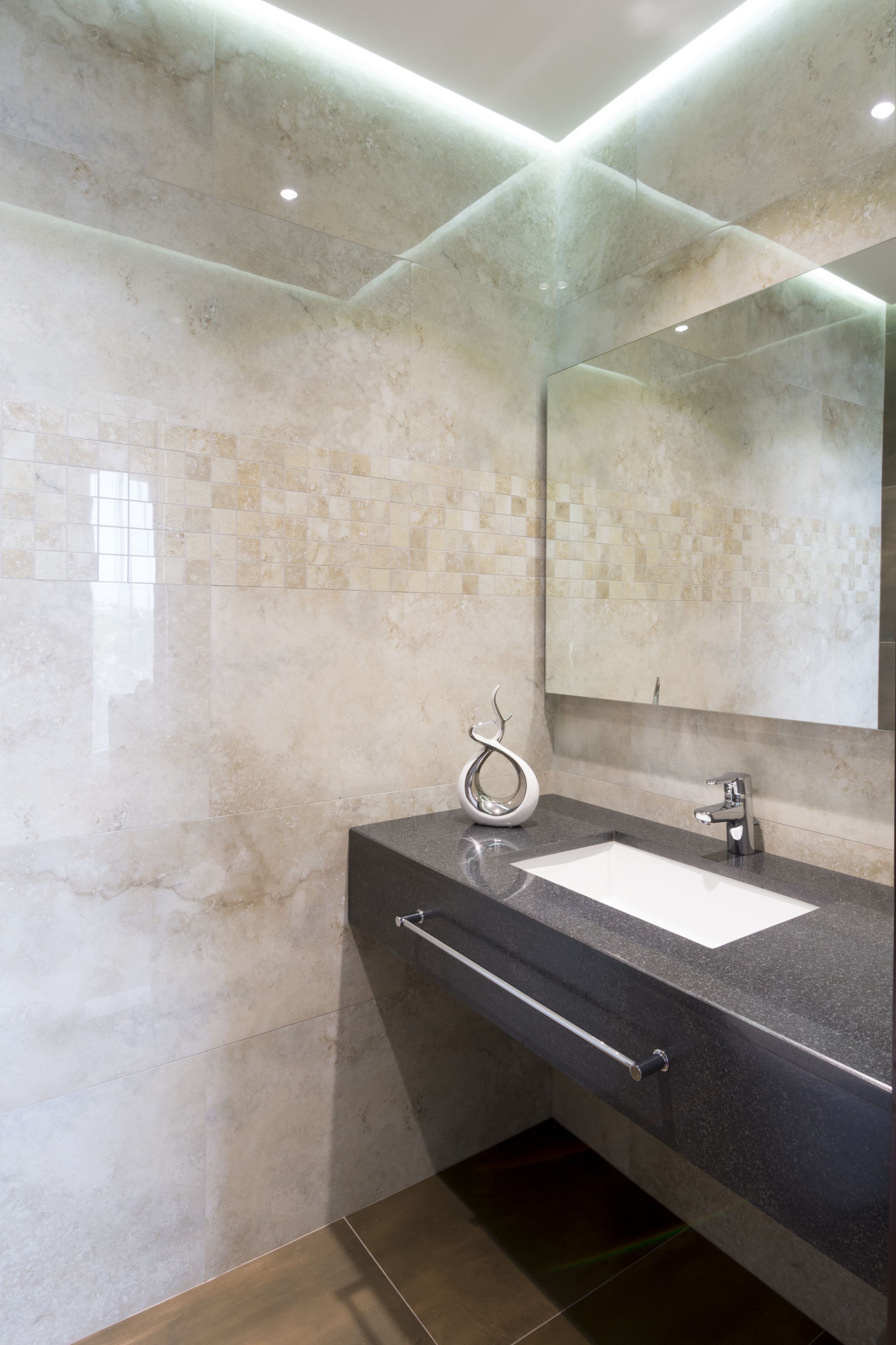 Un baño moderno con pared de mármol, un espejo grande, un lavabo blanco y una encimera elegante.