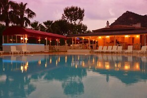 A pool area with lounge chairs and a covered seating area, surrounded by palm trees and a mountain in the background. - White Hotel (Fethiye)