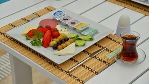 Pöydällä on lautanen, jossa on viipaloituja kurkkuja, tomaatteja, oliiveja, juustoa ja lihaa. Lisäksi tarjolla on pieniä kuppeja dippikastikkeita varten ja lasi teetä.