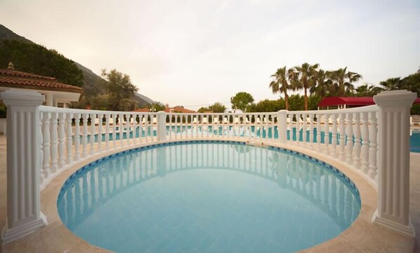 Una piscina circular con barandilla blanca, rodeada de palmeras y montañas al fondo.