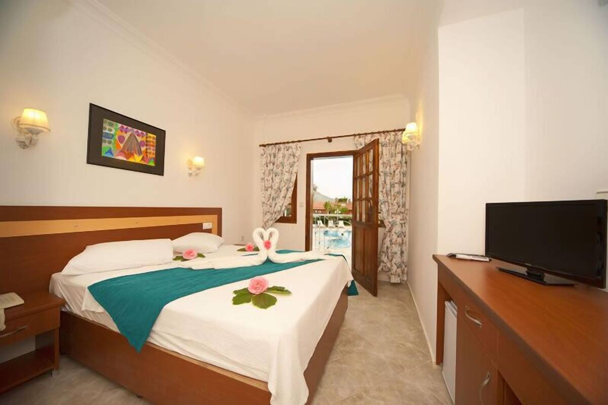 Una habitación de hotel con cama, televisión, escritorio y ventana con cortinas.
