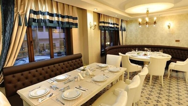 Un coin repas avec une longue table dressée pour quatre personnes, un banc marron rembourré et une table ronde recouverte d’une nappe blanche.