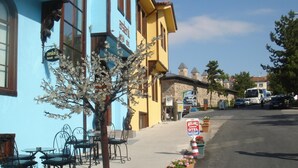Un bâtiment à la façade bleue, une enseigne indiquant l’hôtel Arslanli Konak, des tables et chaises en métal disposées à l’extérieur, et un arbre aux fleurs blanches.