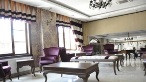 Une pièce spacieuse avec un grand miroir, deux fauteuils violets, une table basse en bois et un papier peint à motifs.