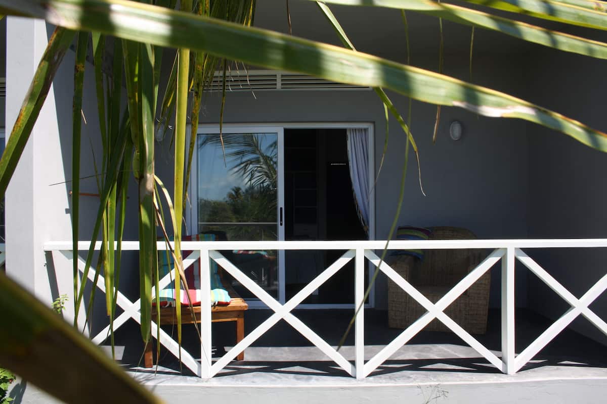 A white balcony with a white railing, a wicker chair, and a small table.