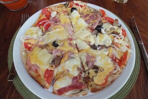 A pizza with various toppings on a white plate. - Casa Jules (Vilanculos)