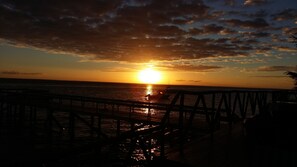 A sunset over the ocean with a wooden pier in the foreground. - Casa Jules (Vilanculos)