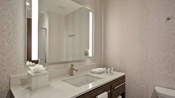 A modern bathroom with a large mirror, two sinks, a towel rack, and a toilet.
