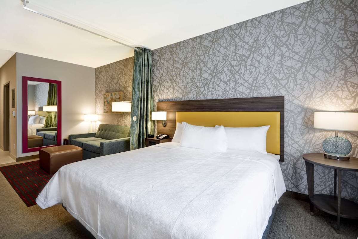 A hotel room with a large bed, a sofa, a desk, and a mirror.