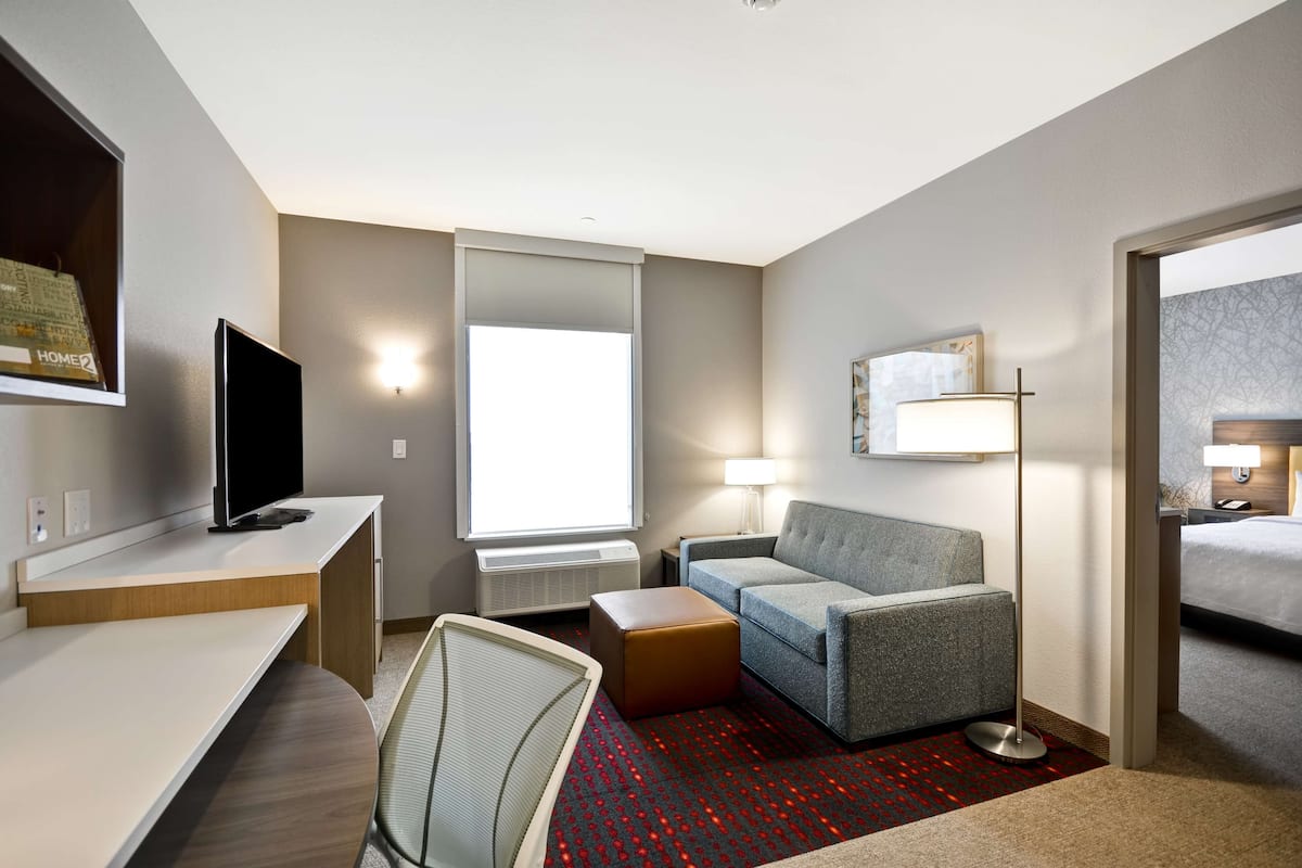A hotel room with a desk, a flat-screen TV, a sofa, a lamp, and a bed.