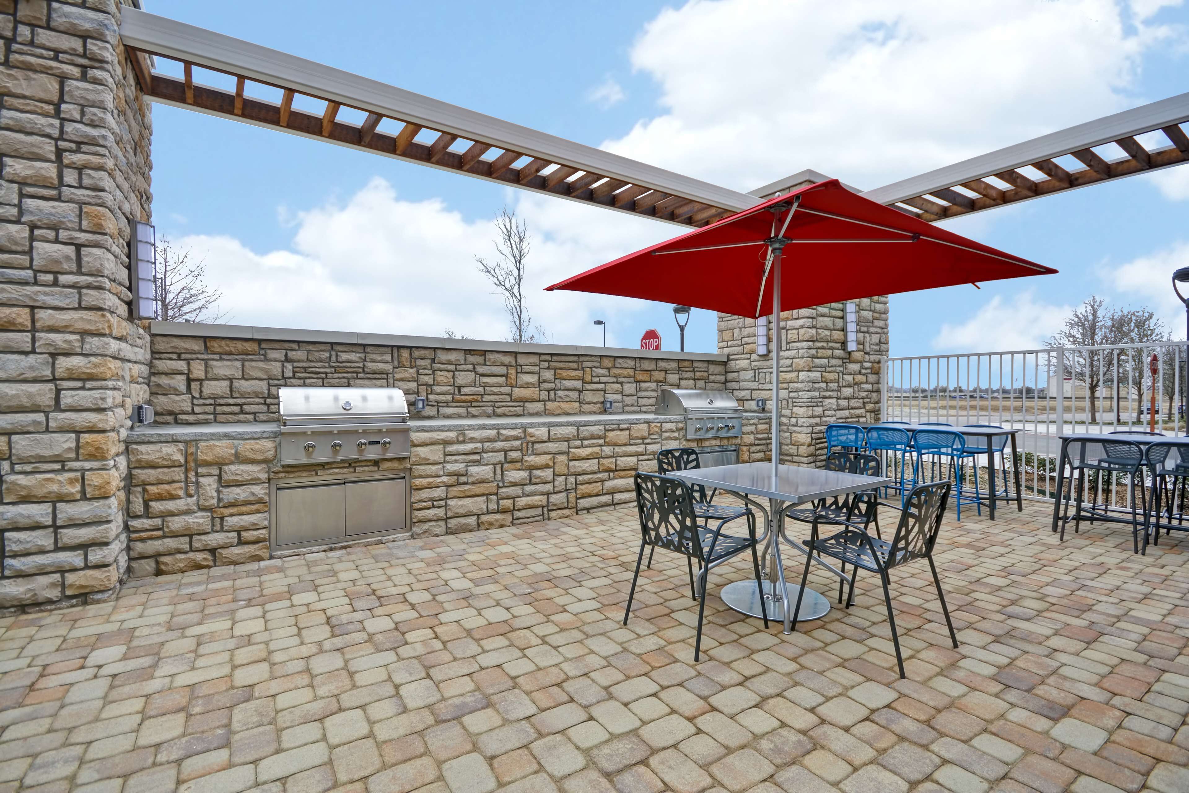 An outdoor patio with stone walls, a grill, and a table with chairs.