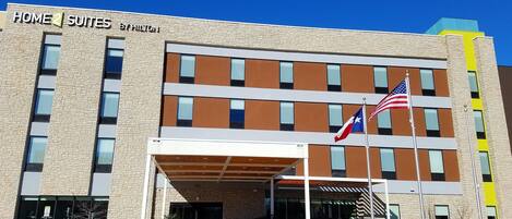 A hotel with a stone facade, multiple windows, and two flags.