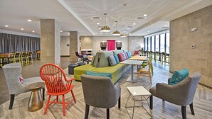 Ein stilvoller Lounge-Bereich mit Sitzgelegenheiten, einer zentralen Couch mit bunten Kissen und einem großen Fenster, das für natürliches Licht sorgt.
