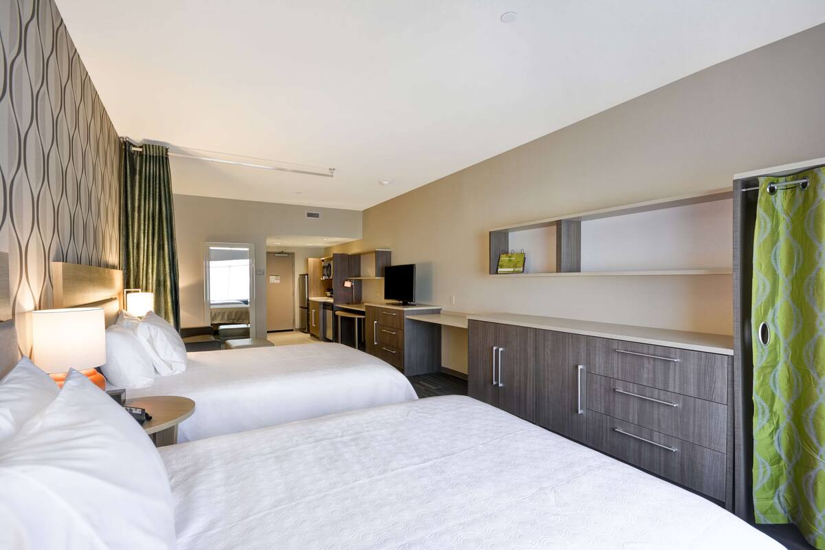 Una habitación de hotel con dos camas, un escritorio, un televisor y una kitchenette.