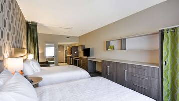 A hotel room with two beds, a desk, a TV, and a kitchenette.
