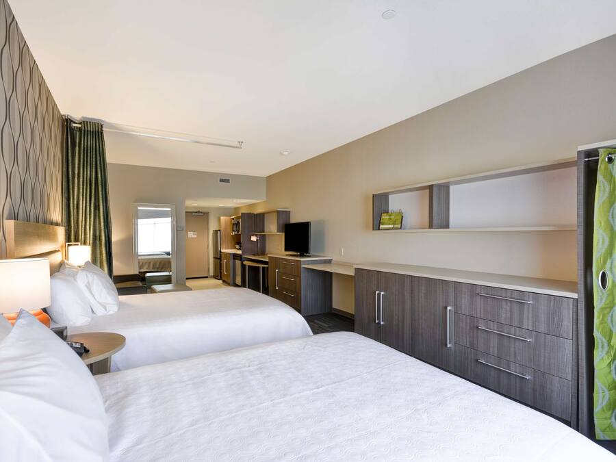 A hotel room with two beds, a desk, a TV, and a kitchenette.