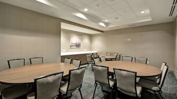 Un salón de conferencias con dos mesas ovaladas grandes, rodeado de sillas, en un entorno hotelero.
