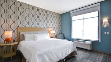 Una habitación de hotel con una cama grande, dos mesitas de noche con lámparas, una ventana con persianas y una pared con un diseño geométrico.