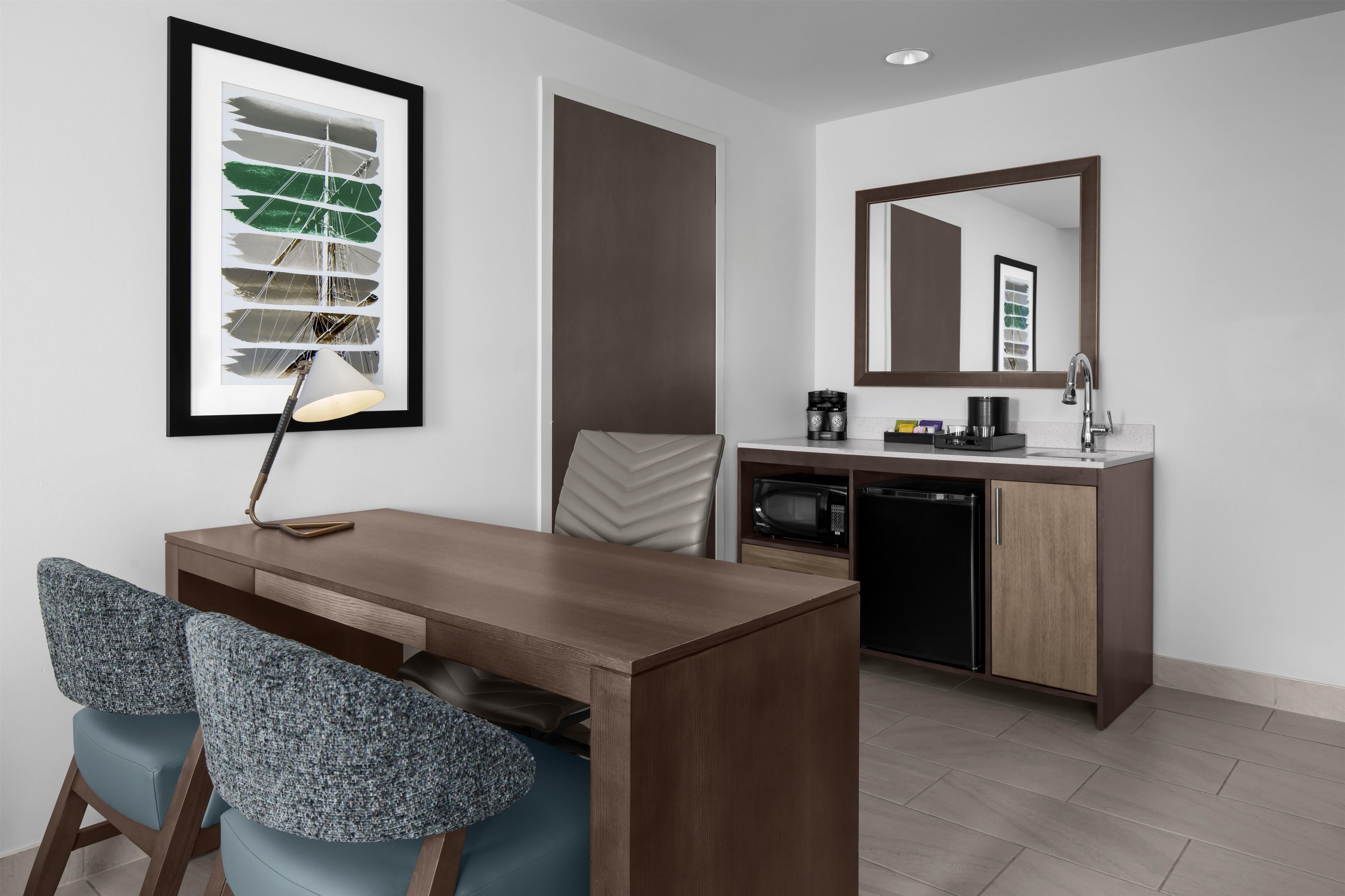 A modern hotel room with a dining area, a kitchenette, and a large mirror.