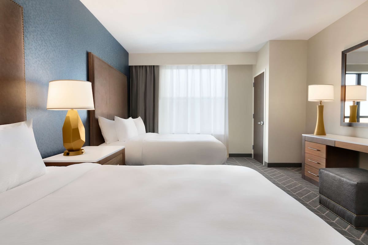 Ein Hotelzimmer mit zwei Betten, einem Schreibtisch, einem Stuhl und einem großen Spiegel.