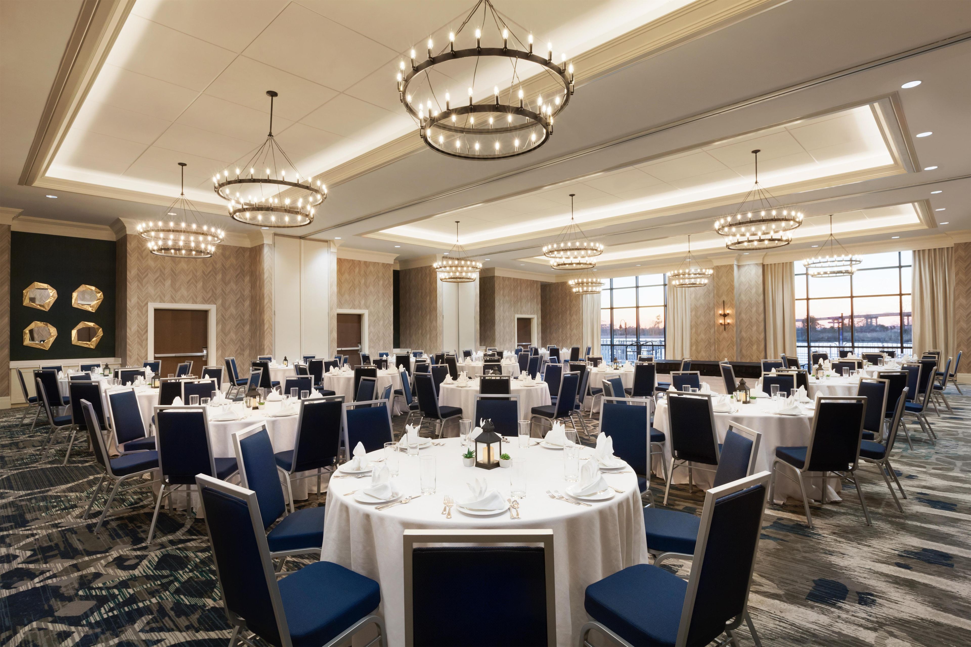 A conference room with round tables, blue chairs, and chandeliers.