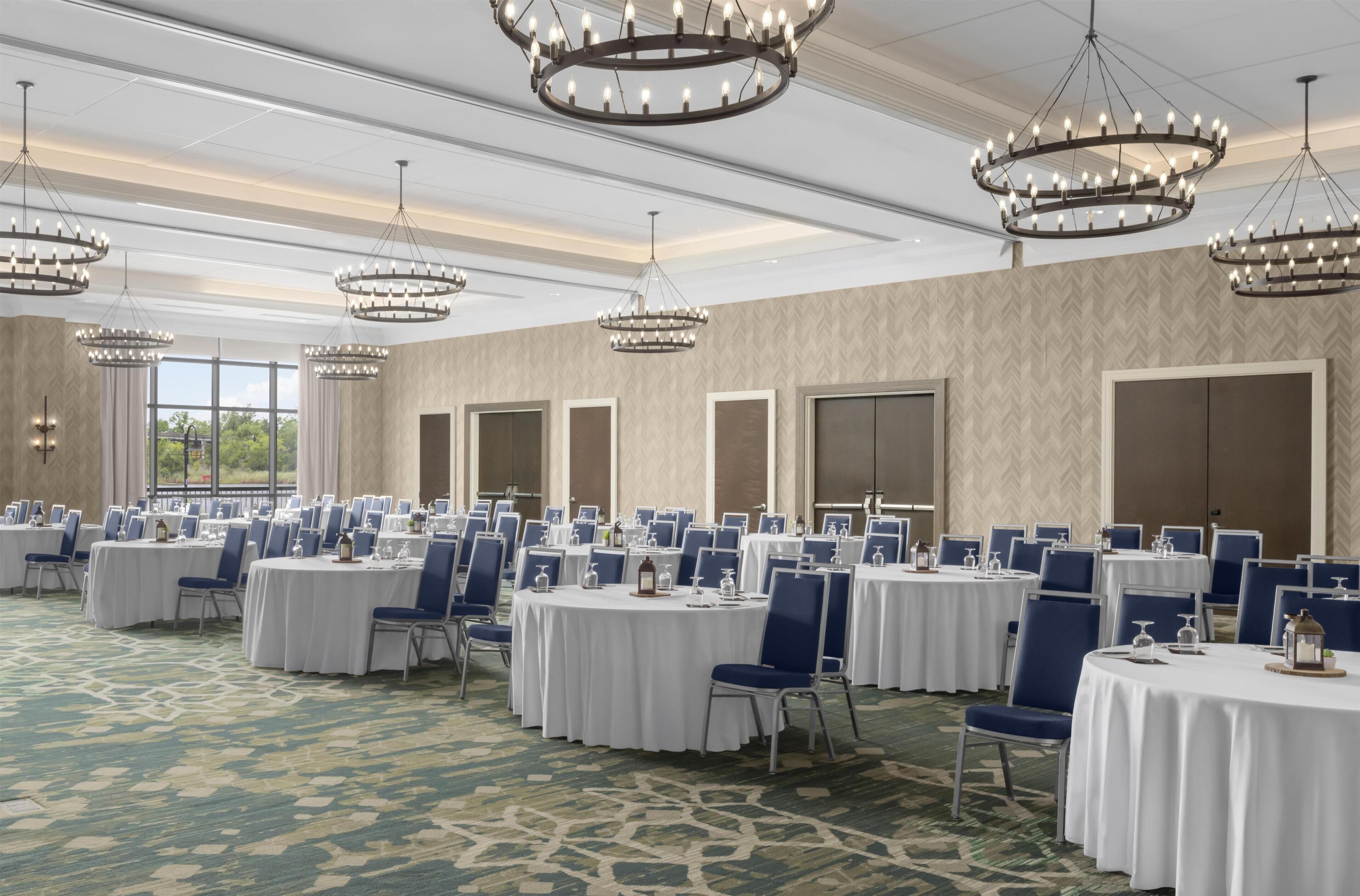 A conference room with round tables, blue chairs, and chandeliers.