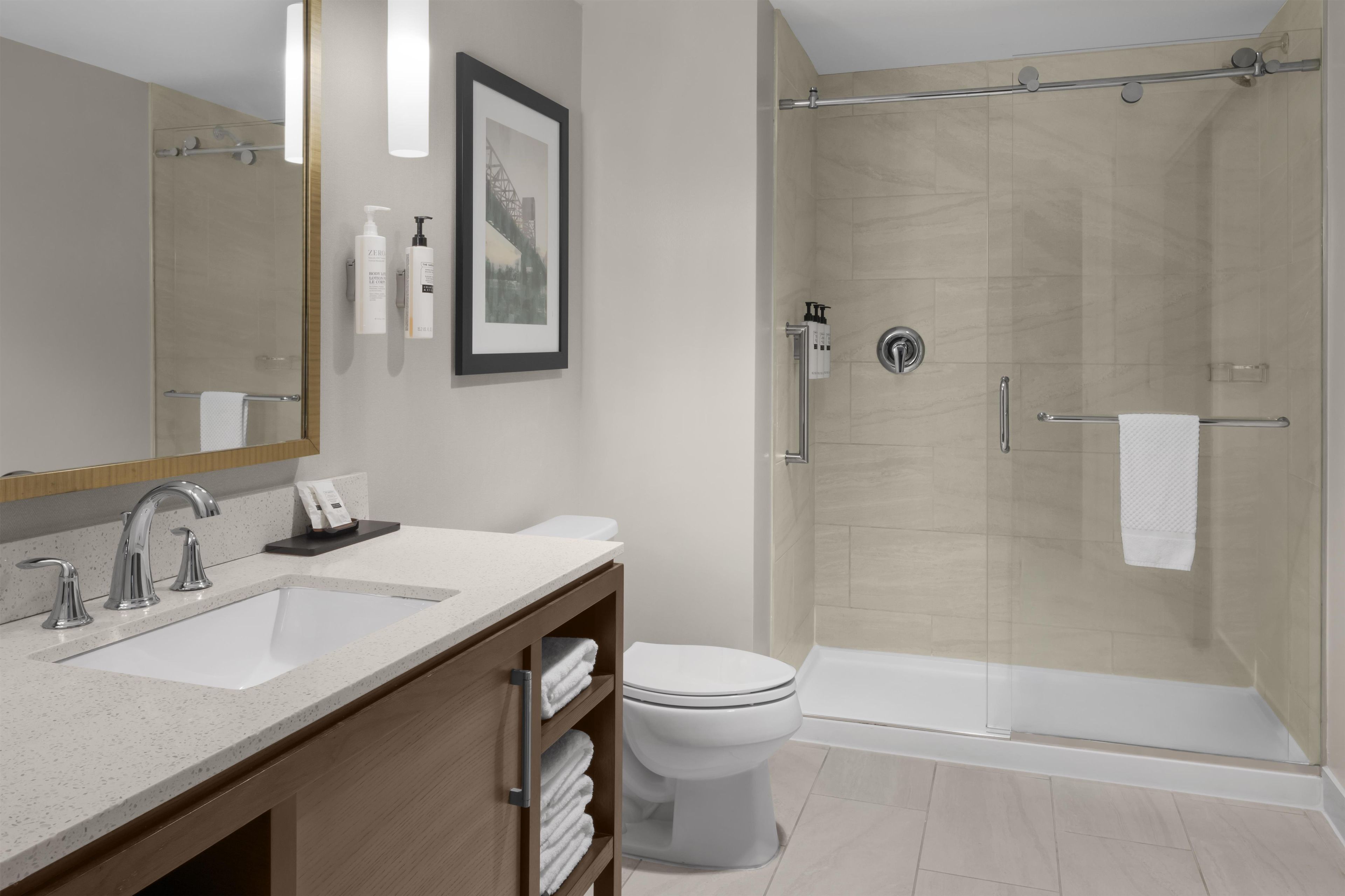 A modern bathroom with a glass-enclosed shower, a large mirror, and a vanity with a sink and toiletries.