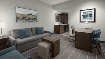 Una habitación de hotel moderna con un sofá gris, una mesita, un escritorio y una kitchenette.