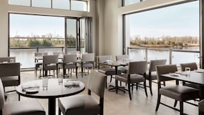 A restaurant with large windows offering views of a body of water and trees. Tables are set with chairs and dining ware. - Embassy Suites by Hilton Wilmington Riverfront (Wilmington)