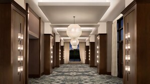 A hotel corridor with a patterned carpet, wooden doors, and a large chandelier. - Embassy Suites by Hilton Wilmington Riverfront (Wilmington)