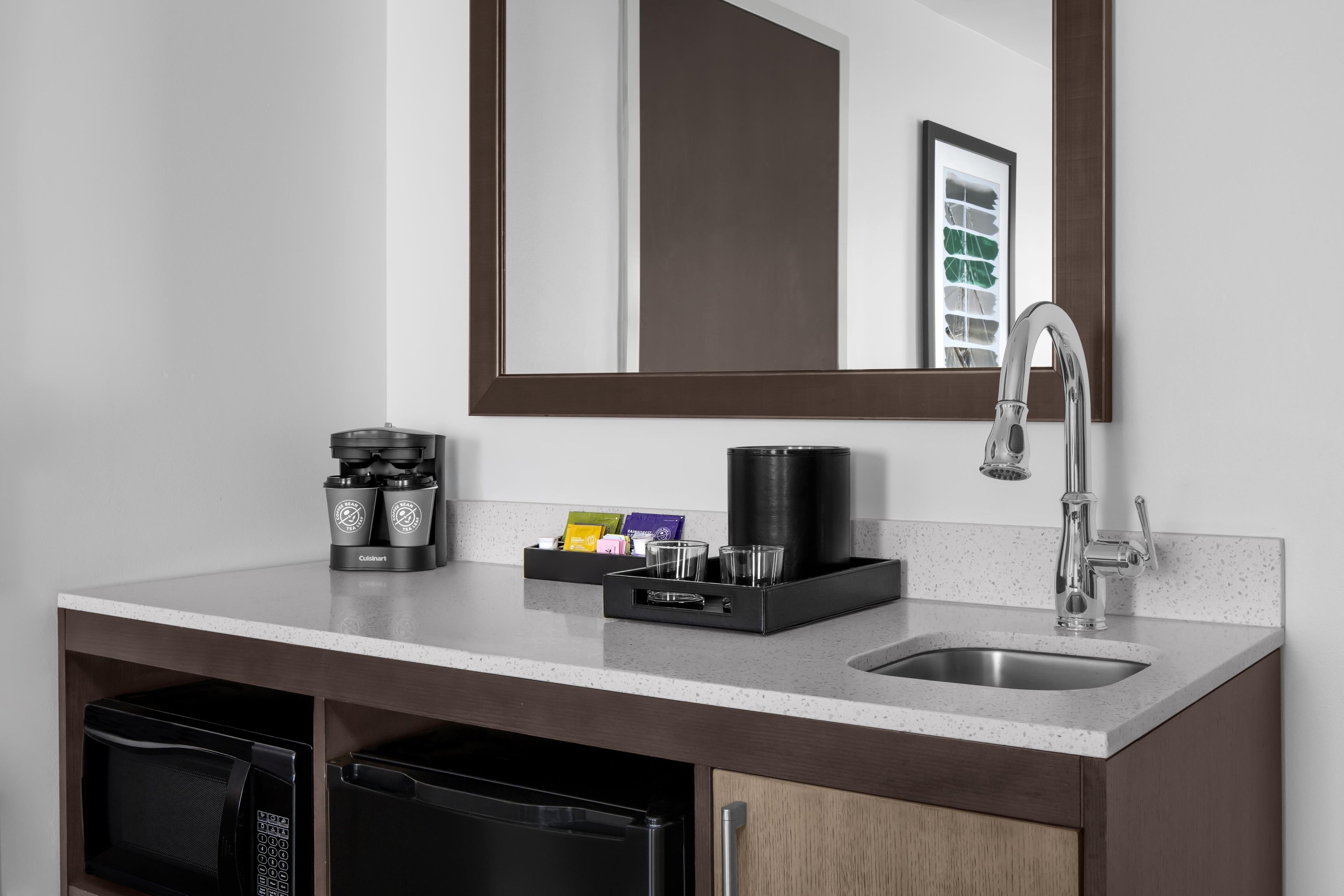 A modern bathroom with a countertop, a sink, a mirror, and a coffee maker.