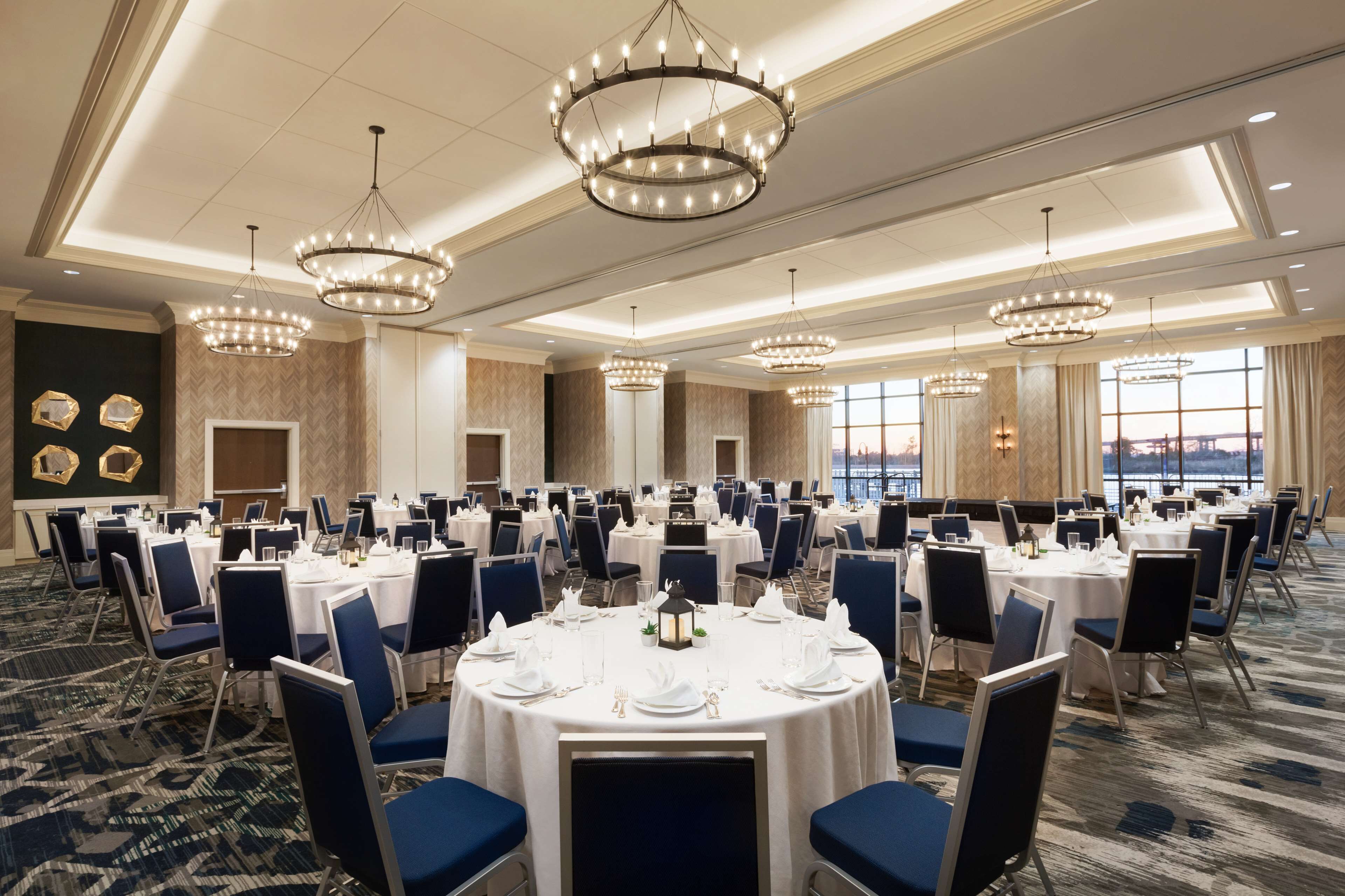 Un salón de banquetes con mesas redondas, sillas azules, candelabros y vistas al agua.