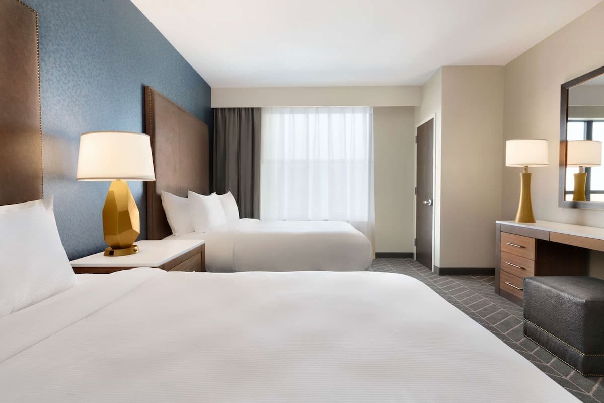 A hotel room with two beds, a desk, a chair, a large mirror, and a window with curtains.