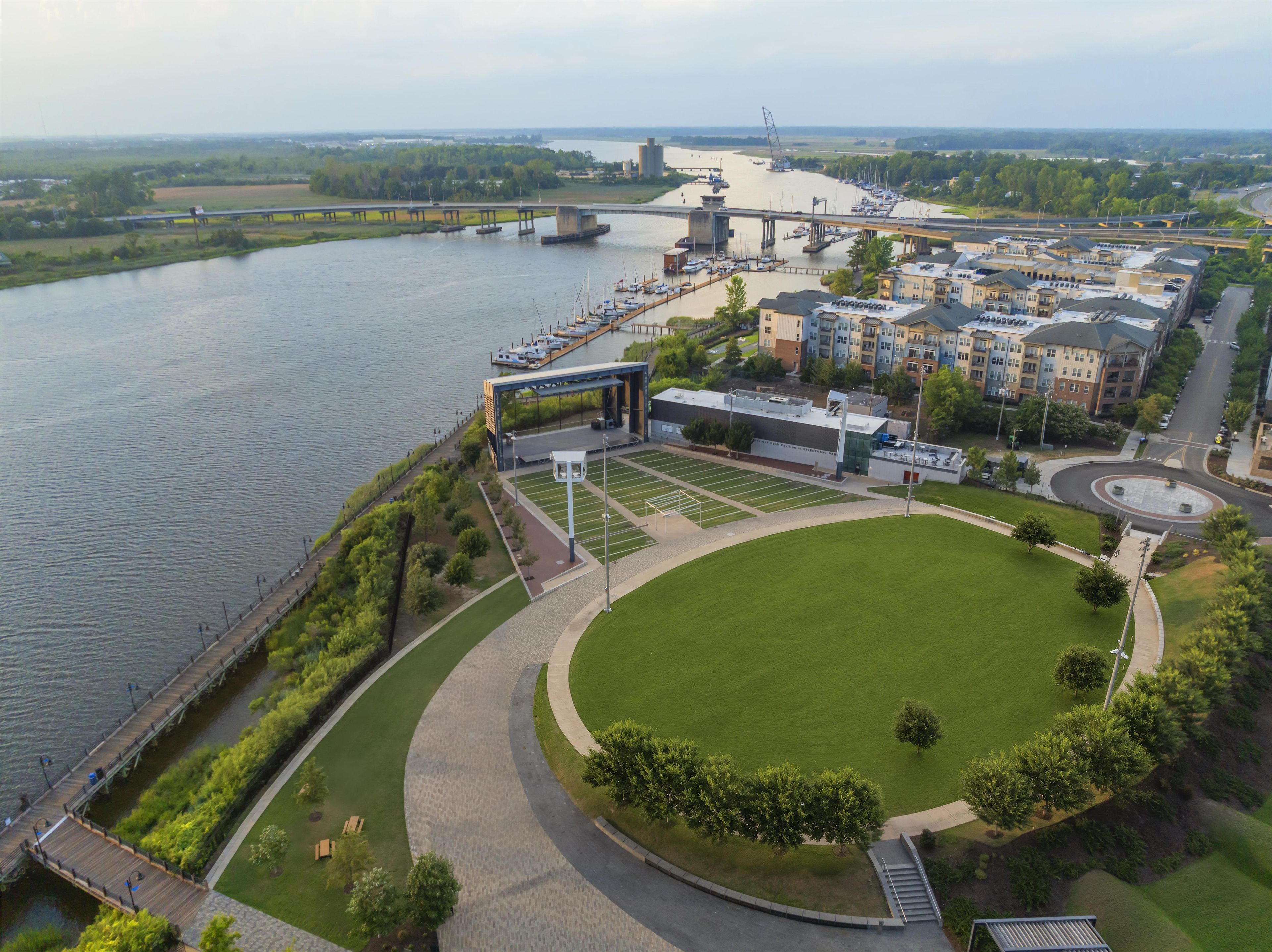 Un parco lungo il fiume con un campo da calcio, un ponte e edifici residenziali.