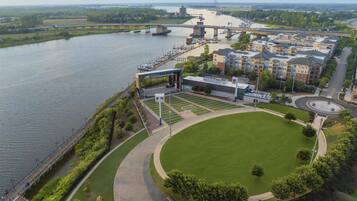 Un parco lungo il fiume con un campo da calcio, un ponte e edifici residenziali.