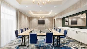 A conference room with a long table, blue chairs, a large mirror, and a patterned carpet.
