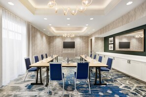 Een vergaderzaal met een lange tafel, blauwe stoelen, een grote spiegel en een kamerbreed tapijt met dessin.
