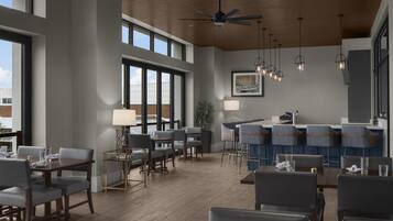 Un comedor moderno con techos altos, ventanas amplias y una variedad de opciones de asientos, incluyendo taburetes y mesas.
