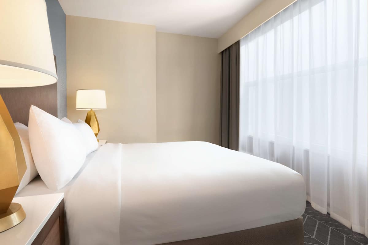 Ein Hotelzimmer mit einem großen Bett, einer Nachttischlampe und durchsichtigen Vorhängen.