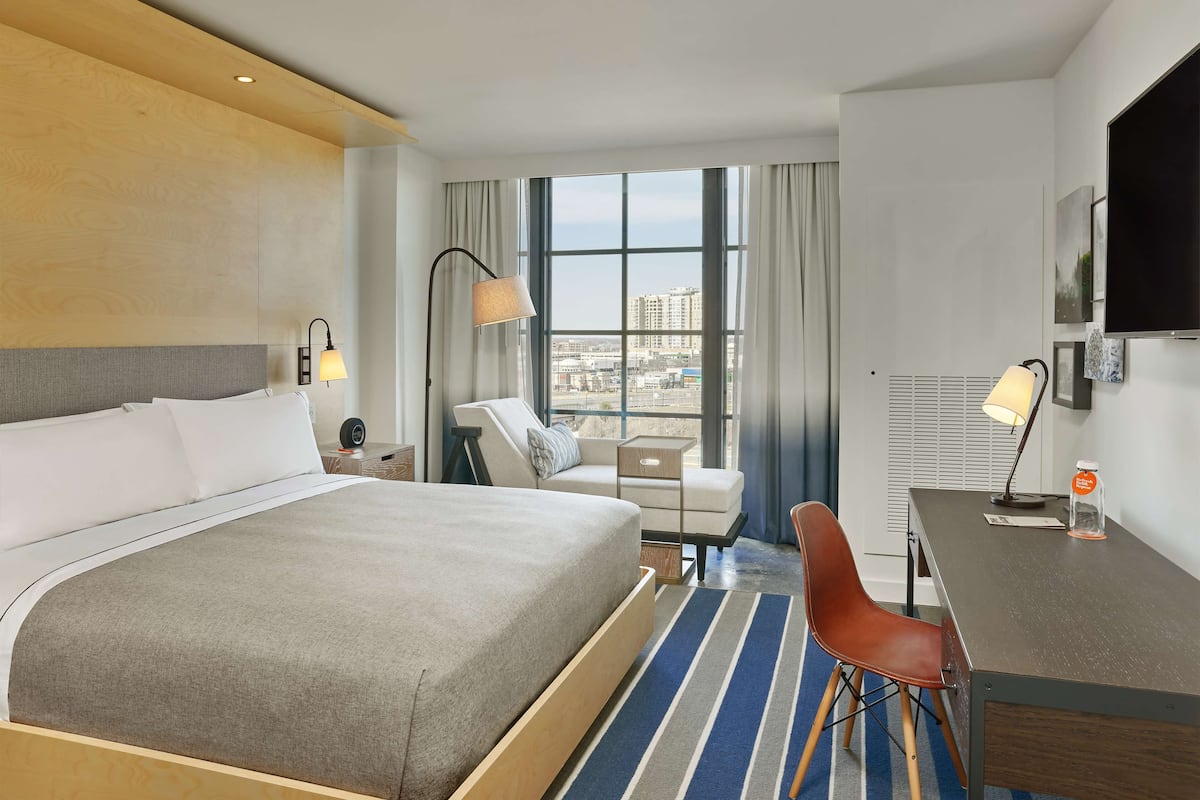 Une chambre d’hôtel dotée d’un grand lit, d’un bureau, d’une chaise, d’un canapé et d’une grande fenêtre donnant sur la ville.