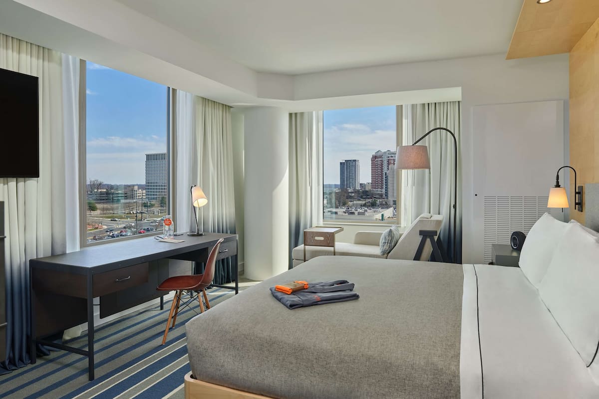 Une chambre d’hôtel avec un grand lit, un bureau, une chaise, une télévision et une vue sur le paysage urbain.